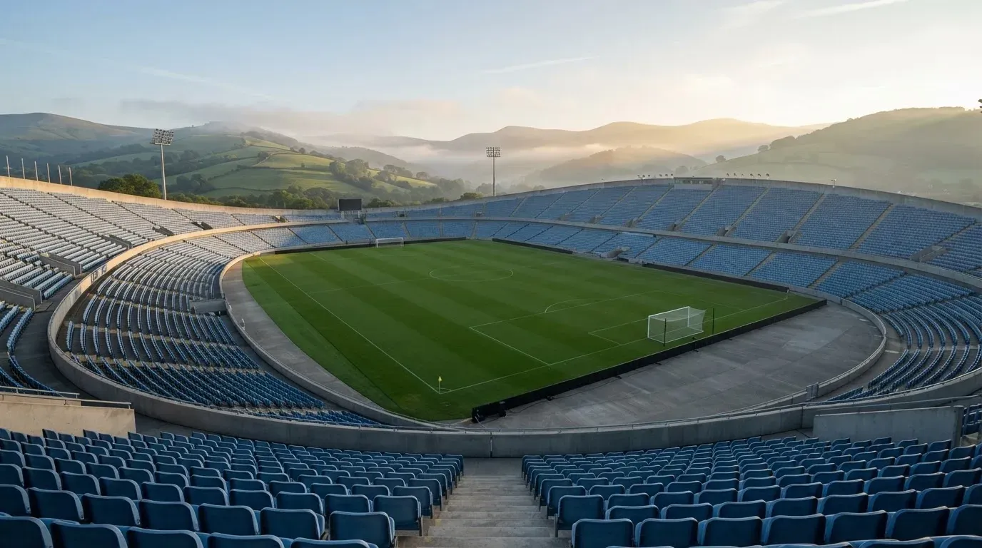 Ein leeres Stadion im Morgenlicht mit Blick auf die Sitzreihen, im Hintergrund Hügel und aufsteigender Nebel.