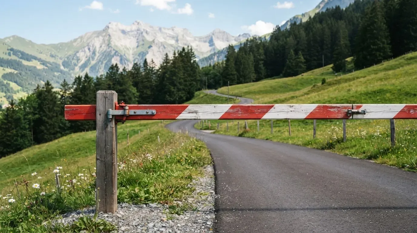Ein Schlagbaum sperrt eine Landstrasse in den Bergen, dahinter windet sich der Weg zwischen grünen Hängen.