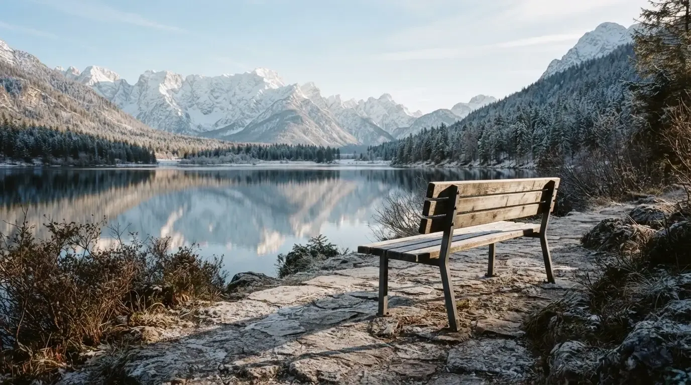 Eine Bank an einem Bergsee, dahinter schneebedeckte Gipfel im klaren Licht eines Wintermorgens.