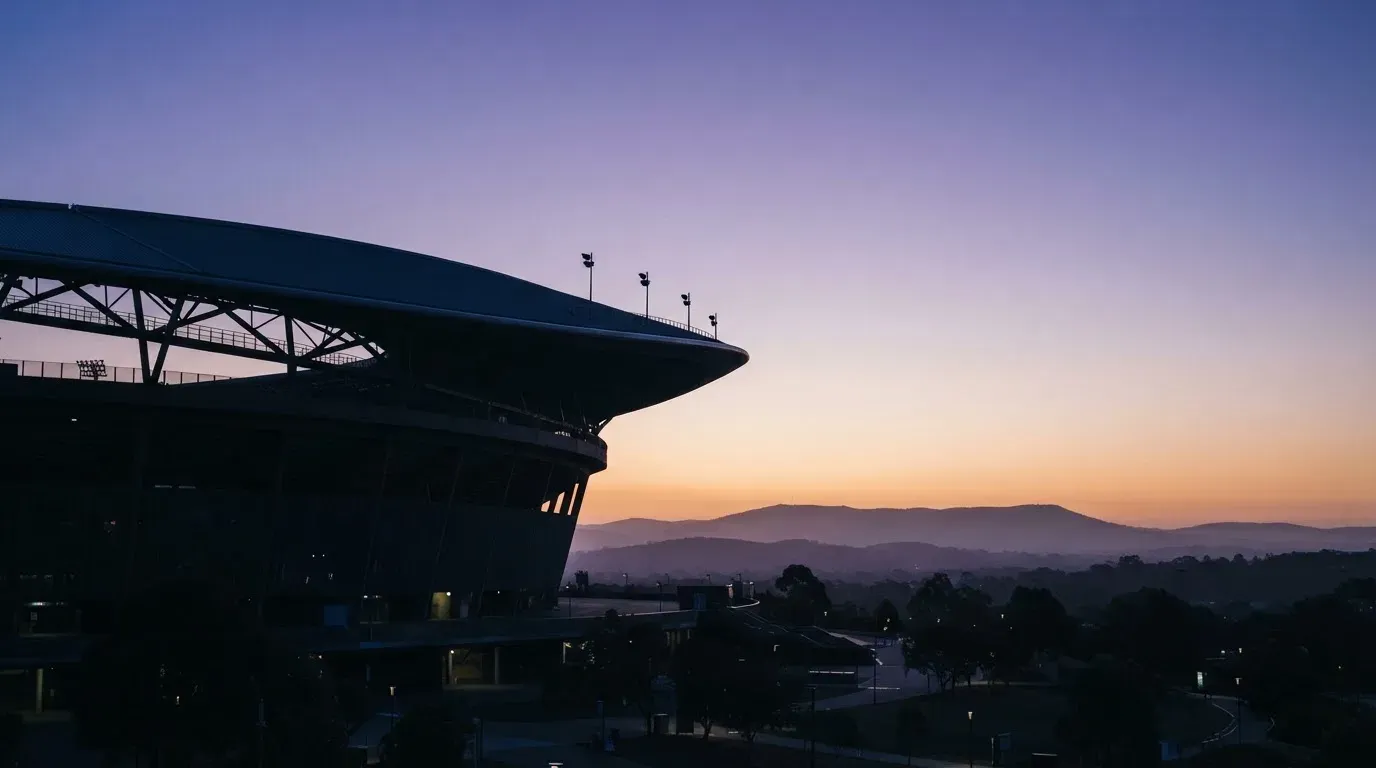 Die Silhouette eines Stadiondachs vor dem violetten Abendhimmel, dahinter eine Hügelkette.