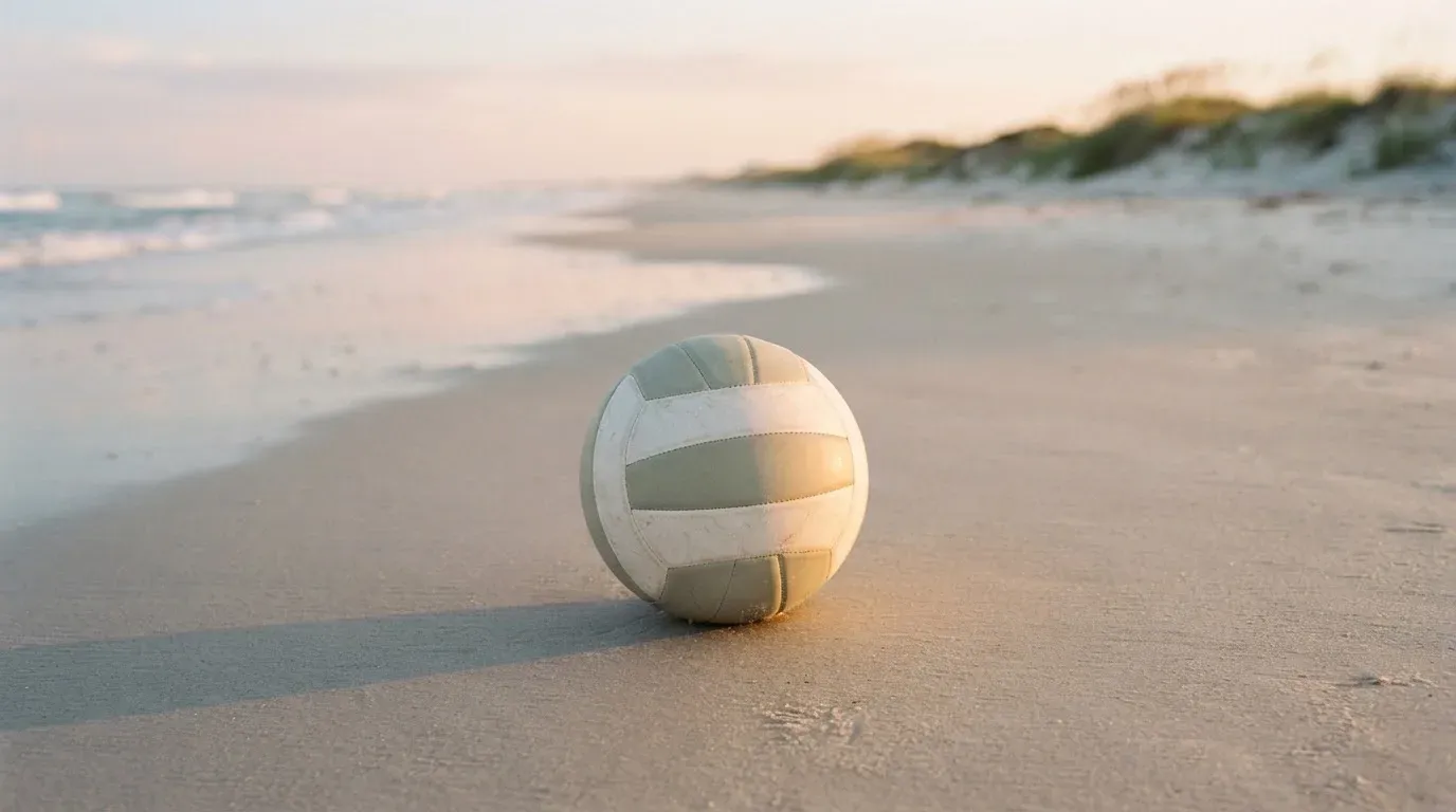 Ein Volleyball liegt auf feinem Sand an einem leeren Strand bei Sonnenaufgang.