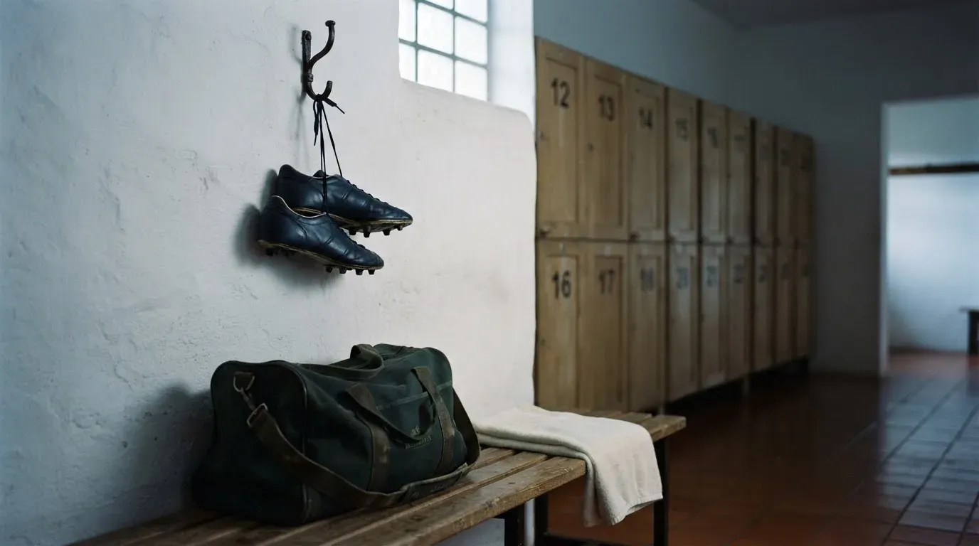 Ein Paar Fussballschuhe hängt an einem Haken in einer ruhigen Umkleide, darunter steht eine Sporttasche auf einer Holzbank.