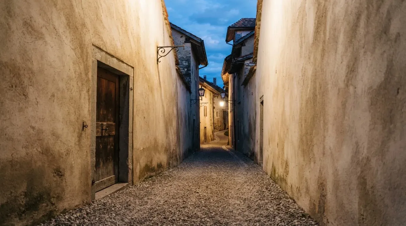 Ein schmaler Kiesweg führt zwischen zwei hellen Mauern durch eine Schweizer Altstadt, die Laternen sind noch nicht angezündet.