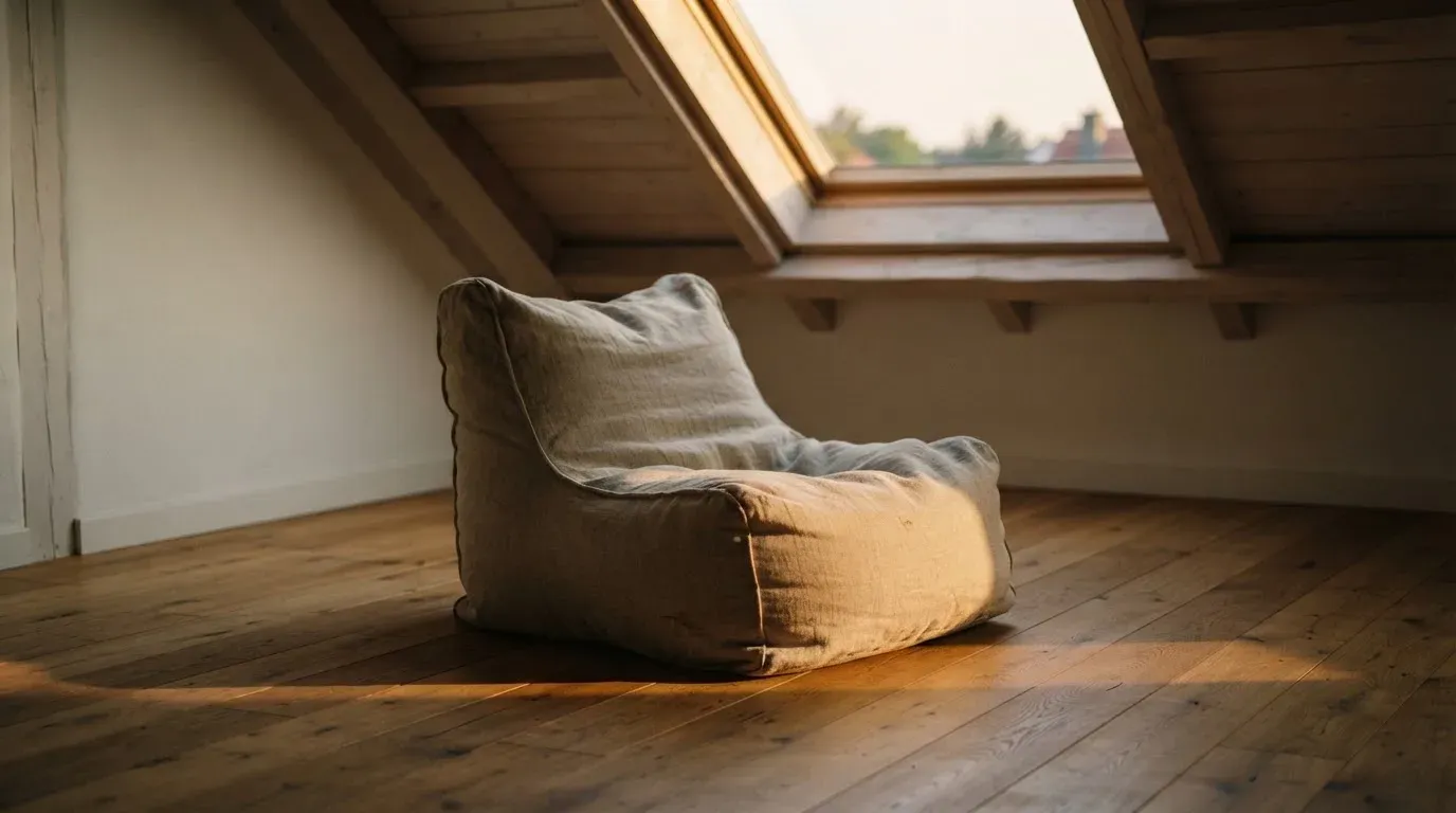 Ein leerer Sitzsack steht in einem Zimmer mit Dachfenster, Abendlicht fällt auf den Holzboden