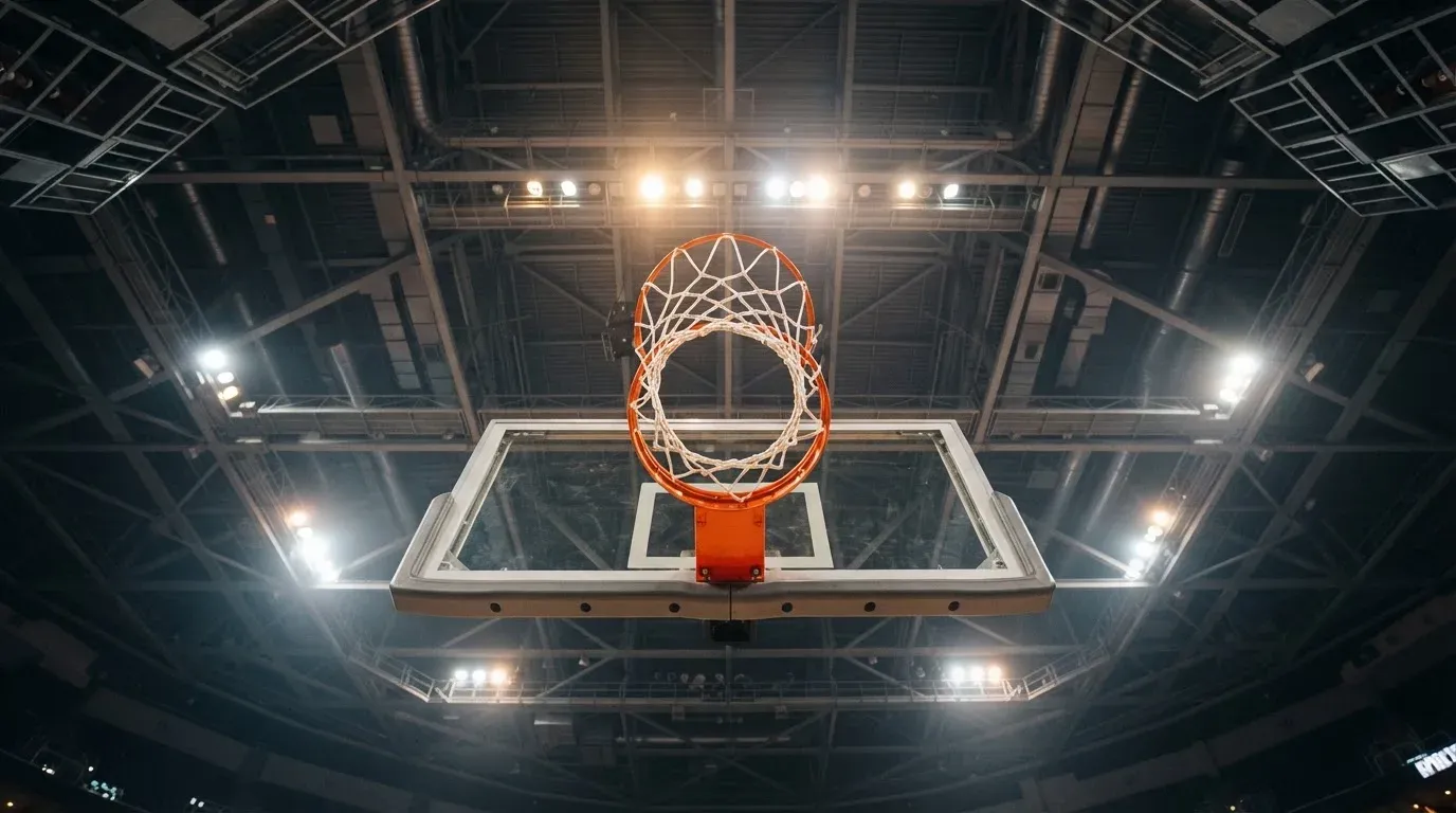 Ein Basketballkorb von unten gesehen, darüber eine Hallendecke mit Scheinwerfern und Stahlträgern.