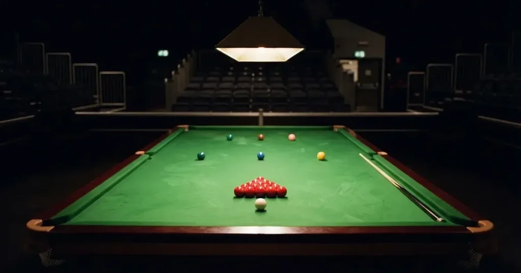 Ein Snookertisch mit grünem Tuch und einem Dreieck aus roten Kugeln unter einer tief hängenden Lampe in einer leeren Halle.