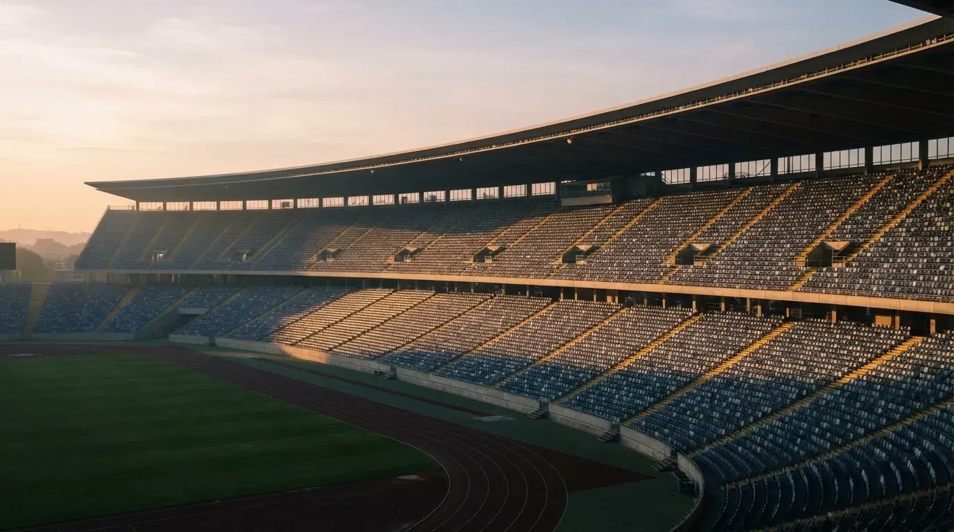 Eine leere Stadiontribüne bei Sonnenaufgang aus der Ferne, lange Schatten fallen über die Sitzreihen