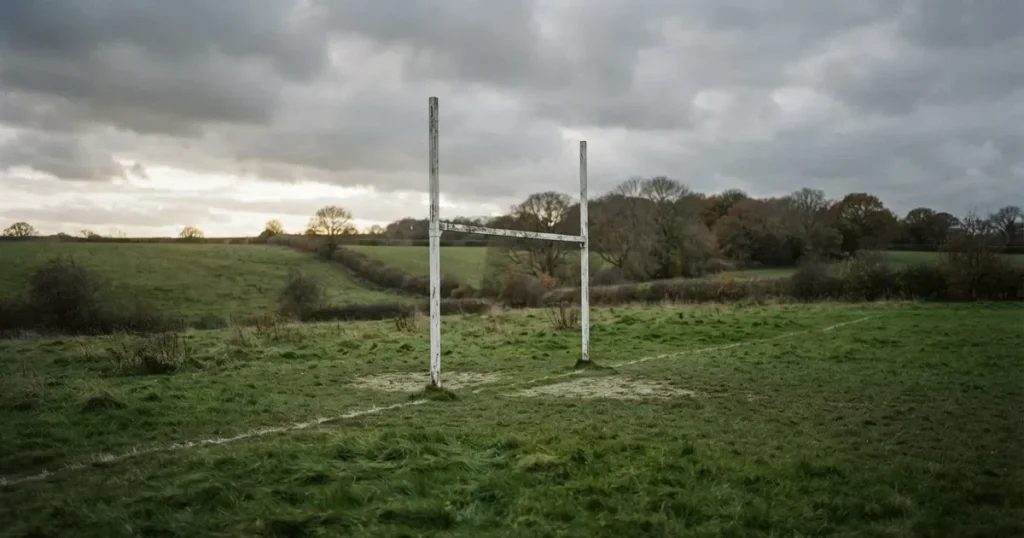 Ein Torpfosten mit Latte steht aus der Ferne vor grauem Himmel auf einer Wiese.