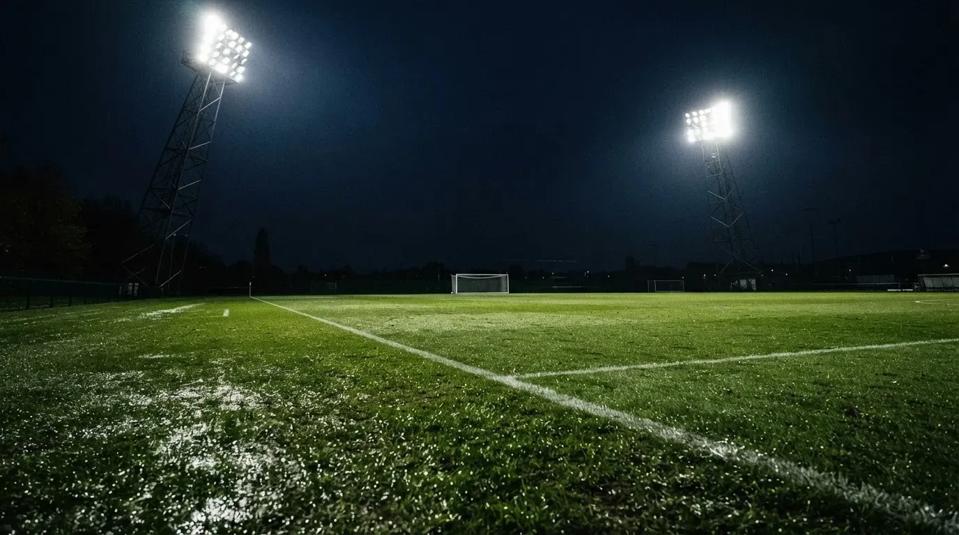 Hohe Flutlichtmasten ragen nachts über einen leeren Trainingsplatz, der Rasen glänzt im weissen Licht.