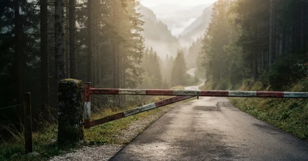 Ein geschlossener Schlagbaum an einer Landstrasse im Gebirge, Morgennebel steht zwischen den Tannen.